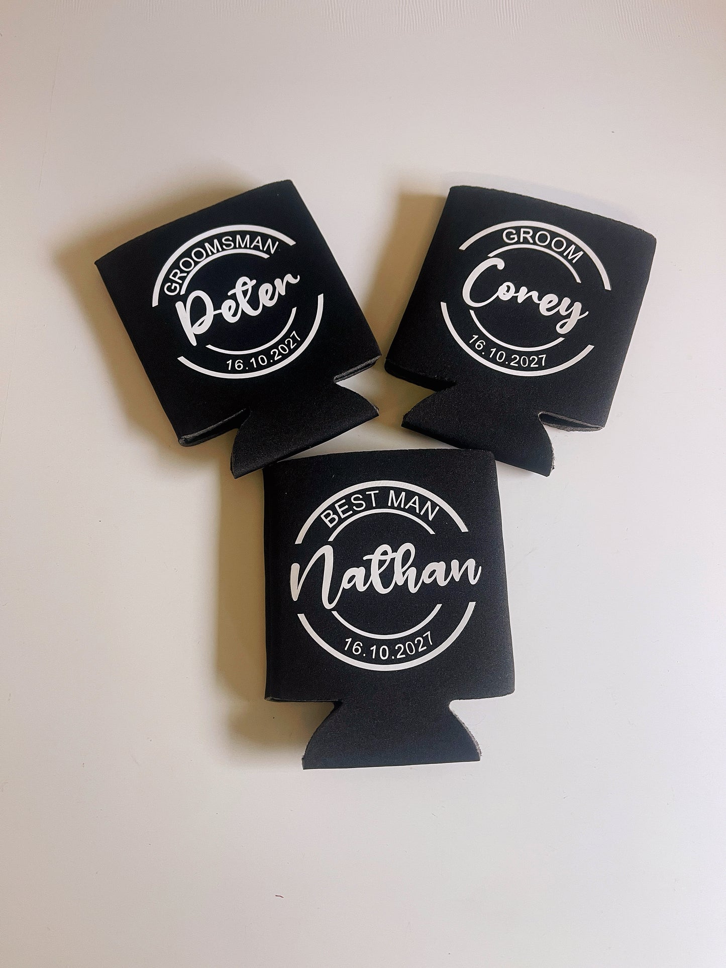 Three black can coolers with personalized names and dates on a white background
