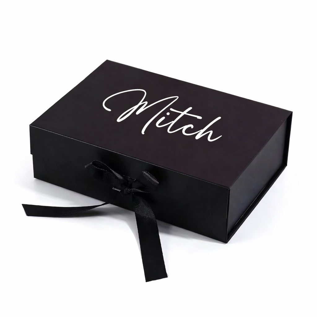 Black gift box with 'Mitch' written on it, tied with a black ribbon on a white background