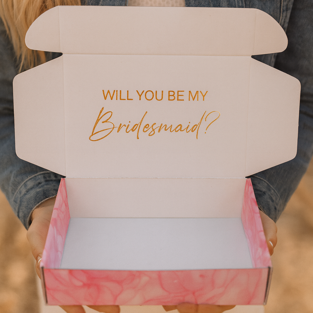 Person holding a box with 'Will You Be My Bridesmaid?' text.