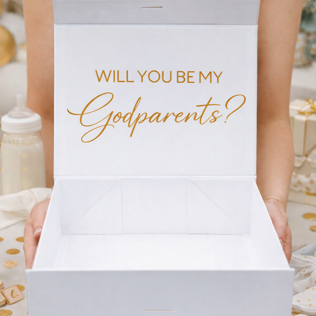 Person holding a white box with 'Will you be my godparents?' text in gold.