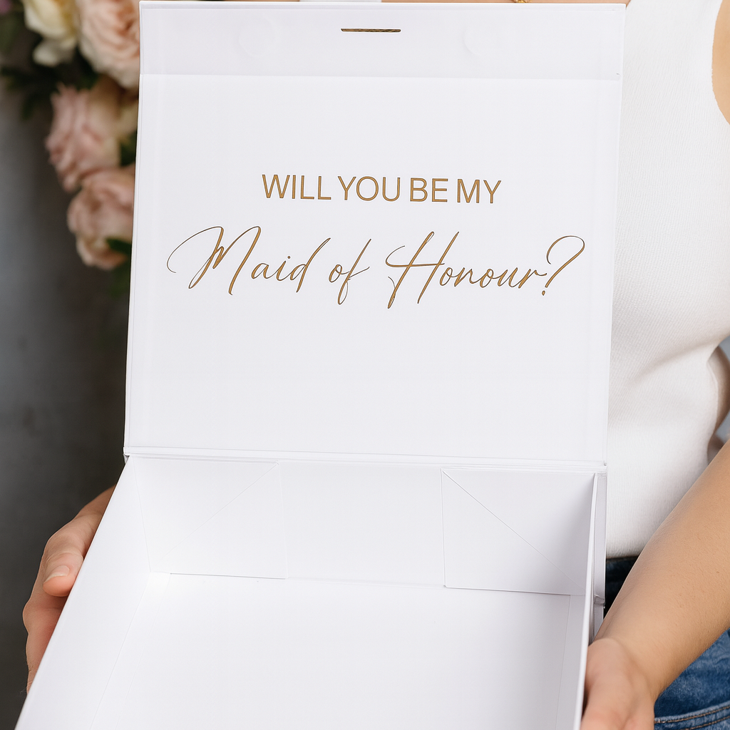 White box with 'Will You Be My Maid of Honour?' text held by a person.
